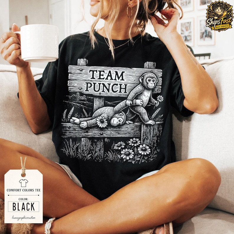 May include: Black Comfort Colors tee with a graphic of two monkeys and the text "TEAM PUNCH" on a wooden sign. The design includes daisies and wheat stalks. The shirt has a tag that says "COMFORT COLORS TEE" and "BLACK".