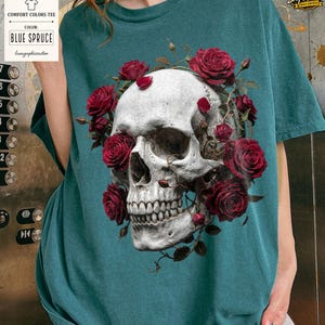 May include: Blue Spruce Comfort Colors tee featuring a detailed skull design adorned with red roses. The graphic tee includes the text "Comfort Colors Tee" and "Blue Spruce". A unique and artistic apparel item.