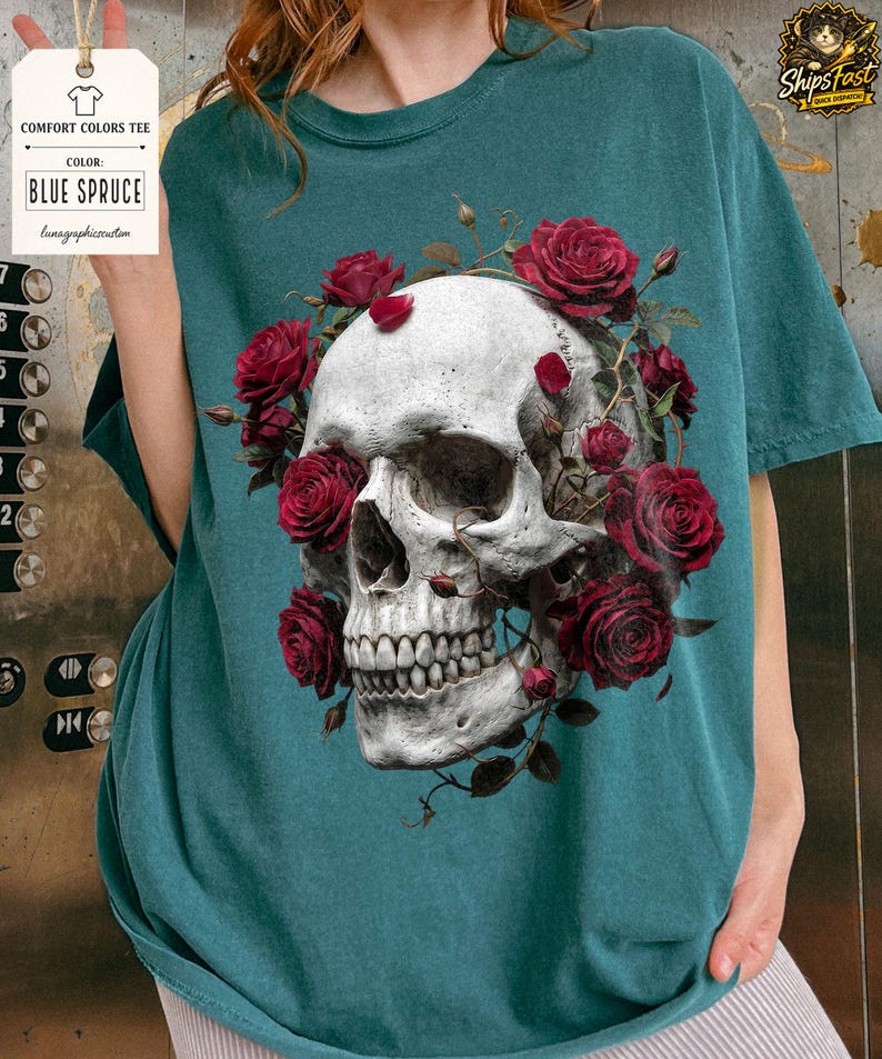 May include: Blue Spruce Comfort Colors tee featuring a detailed skull design adorned with red roses. The graphic tee includes the text "Comfort Colors Tee" and "Blue Spruce". A unique and artistic apparel item.