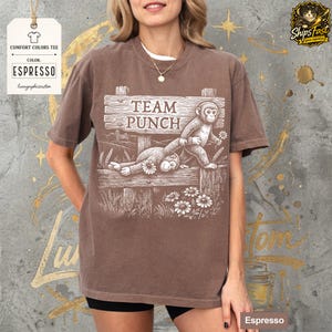 May include: Espresso-coloured Comfort Colors tee featuring a graphic of two monkeys on a wooden fence with the text "TEAM PUNCH". The design includes flowers and wheat stalks. The shirt has a relaxed fit.