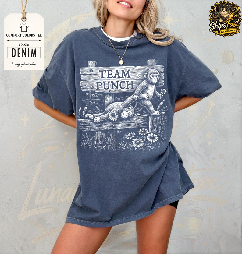 May include: Denim-coloured comfort colours tee featuring a graphic of two monkeys on a wooden fence, with the text "TEAM PUNCH" above. The shirt has a relaxed fit and short sleeves. The design includes flowers and wheat stalks.