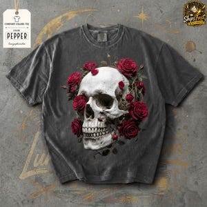 May include: A dark gray Comfort Colors tee featuring a white skull encircled by red roses. The shirt has a vintage look, with the text "Pepper" on a tag. The design is centered on the front of the shirt.