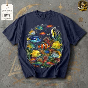 May include: Navy blue Comfort Colors tee featuring a colorful illustration of various fish species swimming around coral. The design includes a clownfish, angelfish, and other vibrant marine life. The tag reads "COMFORT COLORS TEE" and "NAVY".
