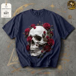 May include: Navy blue comfort colors tee featuring a detailed skull design encircled by vibrant red roses. The shirt includes a tag with the text "COMFORT COLORS TEE" and "NAVY". The design is centered on the front of the shirt.