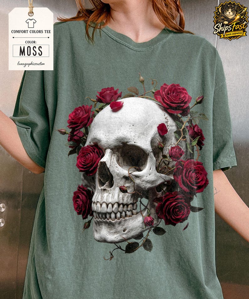 May include: A moss green Comfort Colors tee featuring a detailed skull design encircled by vibrant red roses. The skull has a realistic appearance, and the roses add a contrasting pop of color. The shirt has the text "Comfort Colors Tee" and "Color: Moss".