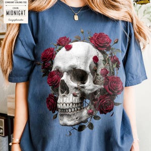 May include: A navy blue Comfort Colors tee featuring a detailed skull design encircled by red roses. The skull is rendered in shades of gray and white, with the roses in full bloom. The shirt includes the text "MIDNIGHT" on a tag.