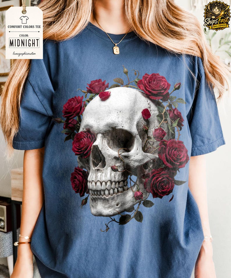 May include: A navy blue Comfort Colors tee featuring a detailed skull design encircled by red roses. The skull is rendered in shades of gray and white, with the roses in full bloom. The shirt includes the text "MIDNIGHT" on a tag.