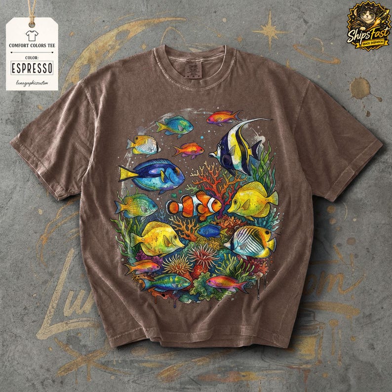 May include: Espresso-colored Comfort Colors tee featuring a vibrant illustration of various colorful fish swimming around coral. The design includes clownfish, angelfish, and other tropical species. The shirt has a relaxed fit and a vintage look.