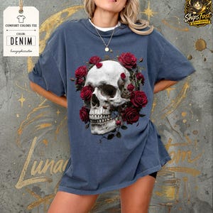 May include: Denim blue Comfort Colors tee featuring a detailed skull design encircled by red roses. The graphic tee includes the text "Comfort Colors Tee" and "Color: Denim". The shirt is from lunagraphicreation.