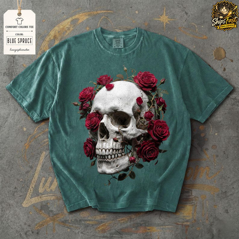 May include: Blue spruce comfort colors tee featuring a detailed skull design encircled by red roses. The graphic tee includes a tag with the text "Comfort Colors Tee" and "Blue Spruce".