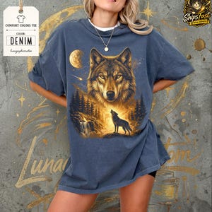 May include: Denim-colored comfort colors tee featuring a detailed illustration of a wolf howling at the moon. The design includes a forest scene with a waterfall and trees. The shirt has the text "Comfort Colors Tee" and "Denim".