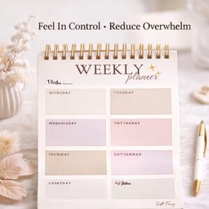 May include: A weekly planner with a gold spiral binding. The planner has a cream-coloured cover with the words "WEEKLY planner" and the text "Feel In Control &bull; Reduce Overwhelm". The planner has sections for each day of the week, with a pen resting on the side.