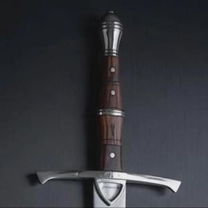 Op de afbeelding: Een middeleeuws zwaard met een donkerhouten handvat en een zilverkleurige pareerstang en pommel. Het handvat is gedetailleerd met zilveren banden en kleine klinknagels. Het lemmet is niet zichtbaar in de afbeelding.