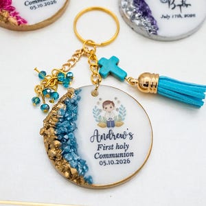May include: Personalised keyrings for First Holy Communion and Baptism. The keyrings feature a round pendant with a gold border, decorated with blue and gold accents. Each keyring has a tassel and a cross charm.