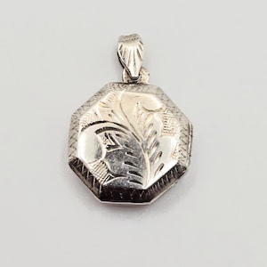 Peut inclure: Un pendentif médaillon octogonal de couleur argentée présentant un motif floral gravé sur la face avant. Le médaillon possède une bordure texturée et comprend une bélière décorative sur le dessus pour l'attacher à une chaîne ou un cordon.