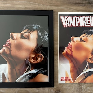 Puede incluir: Impresión enmarcada y cómic con el personaje Vampirella. La obra de arte representa a una mujer con cabello oscuro y sangre alrededor de la boca. La portada del cómic tiene el título "Vampirella".