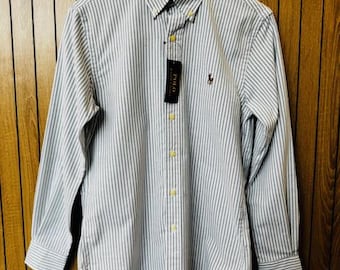 May include: A long-sleeved button-down shirt with vertical blue and white stripes. The shirt has a button-down collar, a small embroidered logo, and a tag that reads "POLO". The shirt is hanging on a wooden hanger.