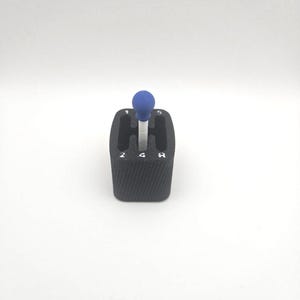 May include: A black gear shift with a blue ball on top. The shift pattern is visible with the numbers 2, 4, and the letter R. The gear shift is set against a white background.