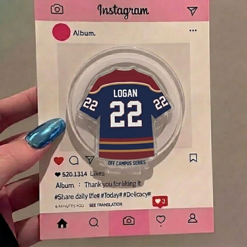 May include: A clear, circular acrylic magnet featuring a navy blue and maroon jersey design with the name "LOGAN" and the number "22". The magnet is set against a pink Instagram-themed background with text and icons.