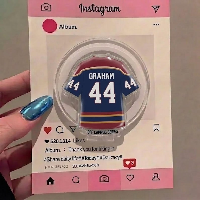 May include: A clear, circular phone grip with a navy blue and maroon jersey design, the name "GRAHAM" and the number "44". The grip is set against a pink Instagram-themed background with text including "Album" and "520.1314 Likes".