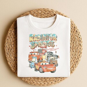 May include: A white ceramic mug with a black handle and the text "But First, Coffee" in a bold, black font. The mug is set against a blurred background, suggesting a cozy setting.