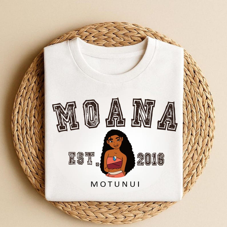 May include: White t-shirt featuring the word "MOANA" in a distressed, dark brown font. Below the word "MOANA" is the text "EST. 2016" and the word "MOTUNUI". A cartoon illustration of a girl with long black hair is in the center.