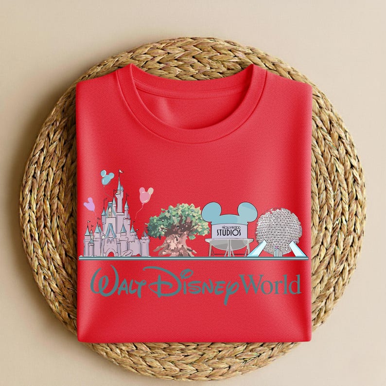 May include: A red crew neck t-shirt featuring a graphic of a castle, tree, film reel, and a sphere, with the text "Walt Disney World" in teal. The design includes Mickey Mouse ears and the word "Studios".