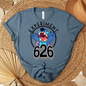 May include: A blue t-shirt with a cartoon character and the text "EXPERIMENT 626". The character is blue with an open mouth and raised arms. The number 626 is in large black numbers.