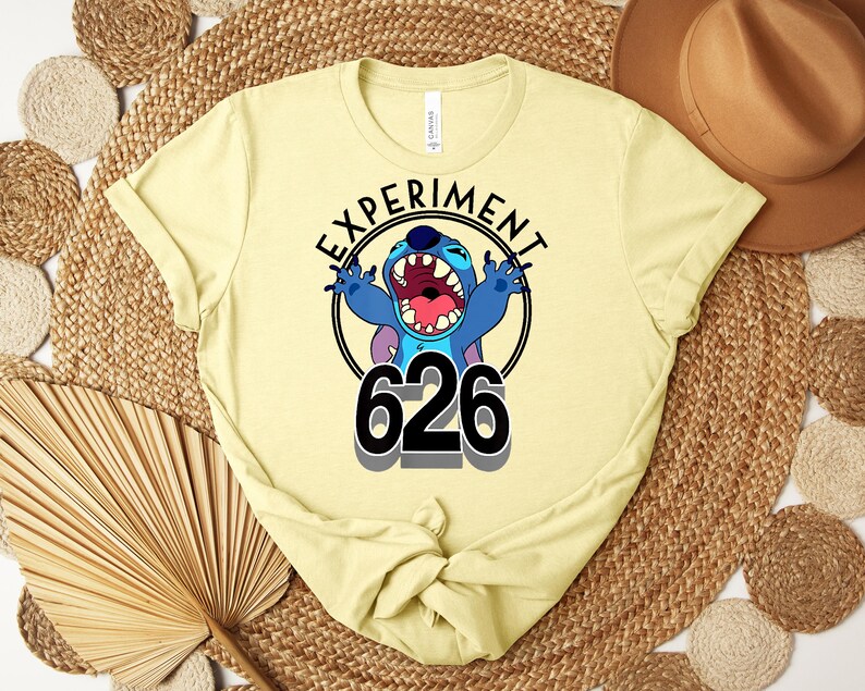 May include: A pale yellow t-shirt with a graphic of the character Stitch from Lilo & Stitch. The design includes the text "EXPERIMENT" above the character and the number "626" below. The character is blue with an open mouth.