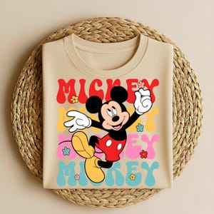 May include: A white ceramic mug with a black handle and the text "But First, Coffee" in a bold, black font. The mug is filled with a dark liquid, likely coffee, and sits on a light-colored surface.