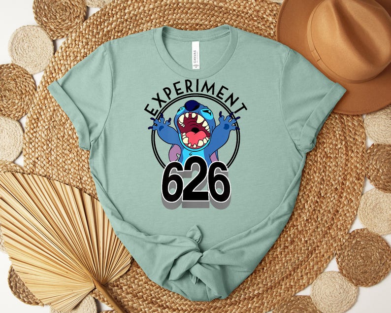 May include: A pale green t-shirt with a graphic of the character Stitch. The design includes the text "EXPERIMENT" above the character and the number "626" below. The character is blue with large teeth and is in a screaming pose.