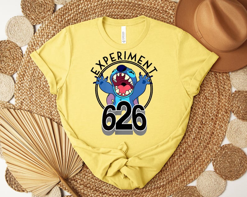 May include: A yellow t-shirt with a graphic of Stitch from Lilo & Stitch. The design includes the text "EXPERIMENT" in a circle around Stitch, with the number "626" below. The shirt is made of a soft material.