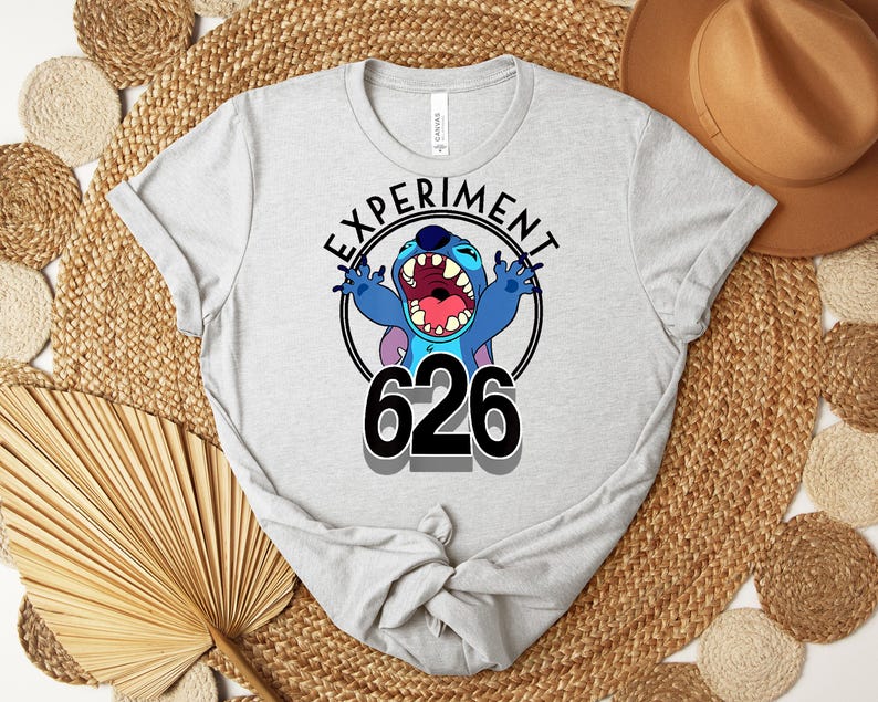May include: Light grey t-shirt with the text "EXPERIMENT 626" and a cartoon character. The character is blue with large ears and an open mouth. The text is in a black circle.