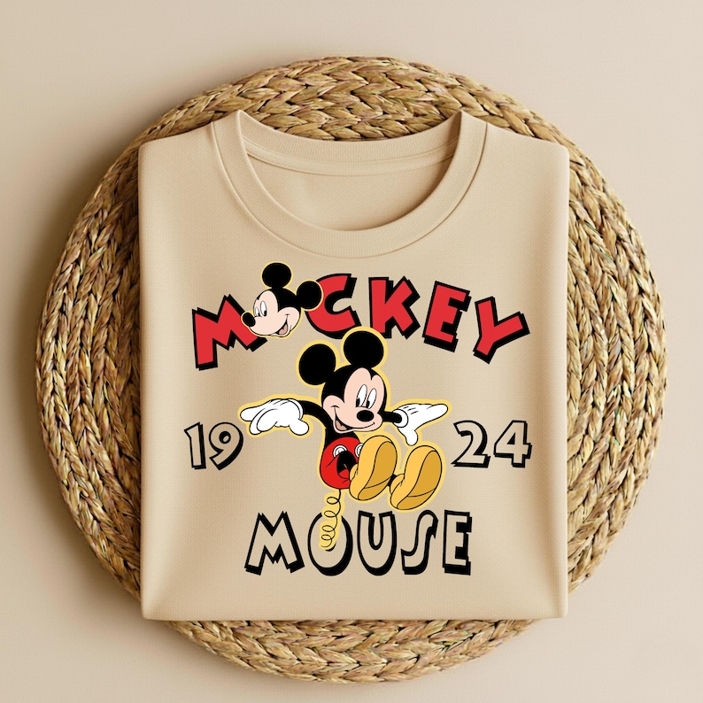 Peut inclure: Sweat-shirt beige &agrave; col rond avec un motif de Mickey Mouse. Le design comprend les mots "Mickey Mouse" en rouge et noir, ainsi que les chiffres "19" et "24". Le personnage de dessin anim&eacute; est au centre.