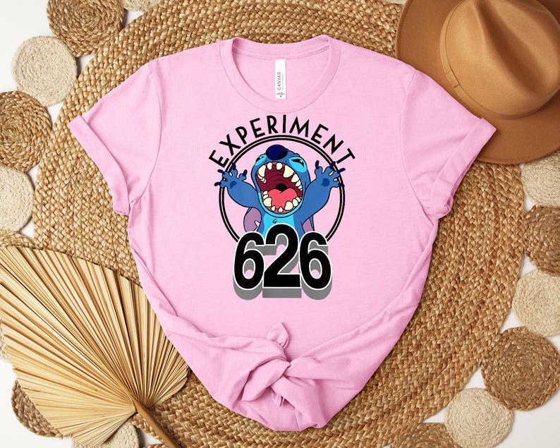 May include: A light pink t-shirt with a graphic of the character Stitch from Lilo & Stitch. The design includes the text "EXPERIMENT" above the character and "626" below. The character is blue with an open mouth.