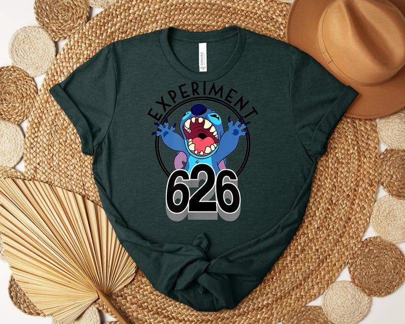 May include: Dark green t-shirt with a cartoon character and the text "EXPERIMENT 626". The character is blue with large ears, an open mouth, and outstretched arms. The shirt is made of a soft material and is suitable for casual wear.
