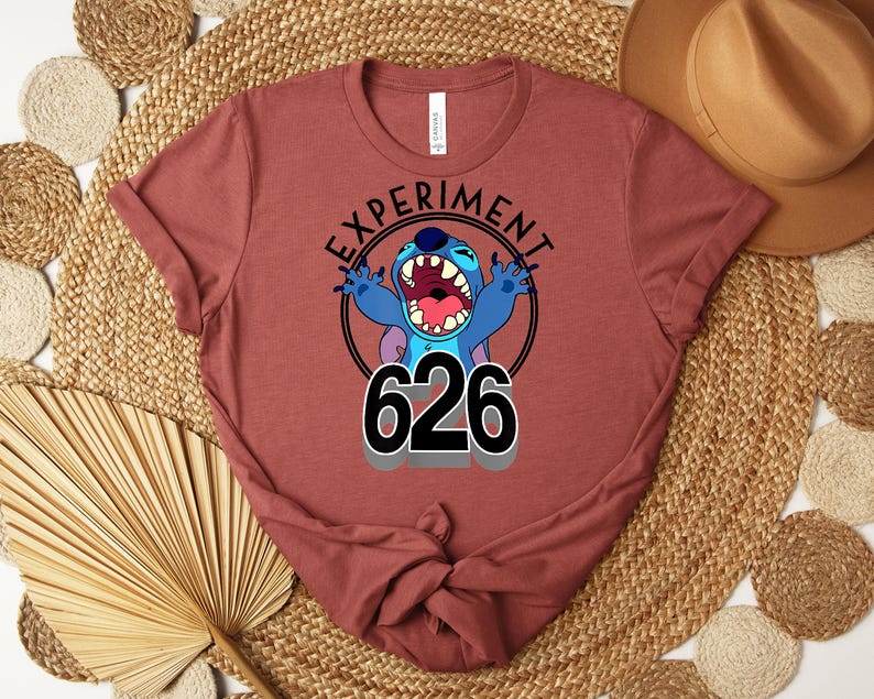 May include: A maroon t-shirt with a graphic of the character Stitch. The design includes the words "EXPERIMENT" and "626" in black, with Stitch in blue and purple. The t-shirt is folded.