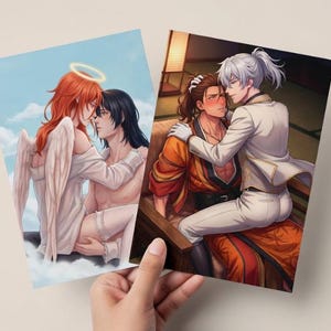 May include: Two rectangular art prints featuring anime-style illustrations. The left print shows a red-haired angel with wings and a halo embracing a dark-haired figure. The right print depicts a white-haired character in a suit sitting on a lap.