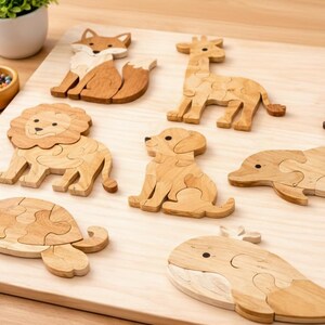 May include: Wooden animal puzzles including a fox, giraffe, lion, dog, dolphin, turtle, whale, and penguin. The puzzles are made of light-colored wood and are arranged on a wooden surface. A small bowl of colorful beads and a potted plant are also present.