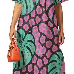 Puede incluir: Vestido hasta la rodilla con fondo negro, con grandes hojas verde azulado y manchas de leopardo rosas y moradas. El vestido tiene mangas cortas y un escote cuadrado. Se sostiene un bolso naranja en la mano. Los tacones amarillos completan el look.