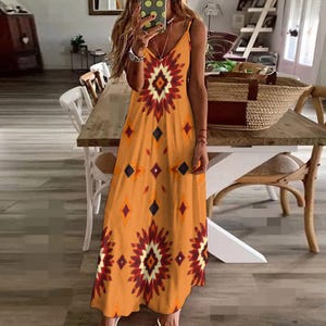 Puede incluir: Un vestido largo naranja con cuello en V y tirantes finos. El vestido presenta un estampado geométrico en tonos rojos, naranjas y negros. El vestido es largo hasta el suelo y adecuado para climas cálidos.