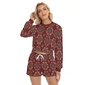 May include: A long-sleeved cropped sweatshirt and matching shorts set featuring a repeating dark red and muted green floral pattern. The shorts include a white drawstring at the elasticated waistband, and the top has a crew neckline.