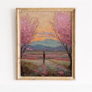 Op de afbeelding: Een ingelijst olieverfschilderij toont een serene landschap. Roze bloesem bomen omlijsten een pad dat leidt naar een figuur voor bergen. De lucht gaat over van oranje naar blauw.