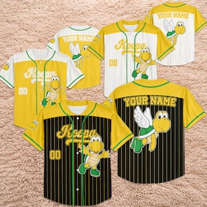 May include: Yellow and black baseball jerseys with the word "Koopa" and the number "00" on the front. The jerseys feature a cartoon Koopa Troopa character and the option to add a name on the back. The jerseys have green and white accents.