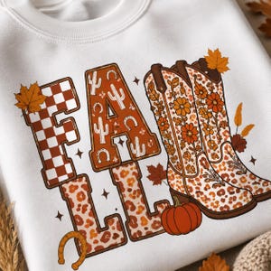 May include: A white sweatshirt featuring the word FALL in large block letters. The F has a brown checkered pattern, the A features cacti and horseshoes, and the Ls have a leopard print. Two cowboy boots with floral and leopard patterns and a pumpkin.