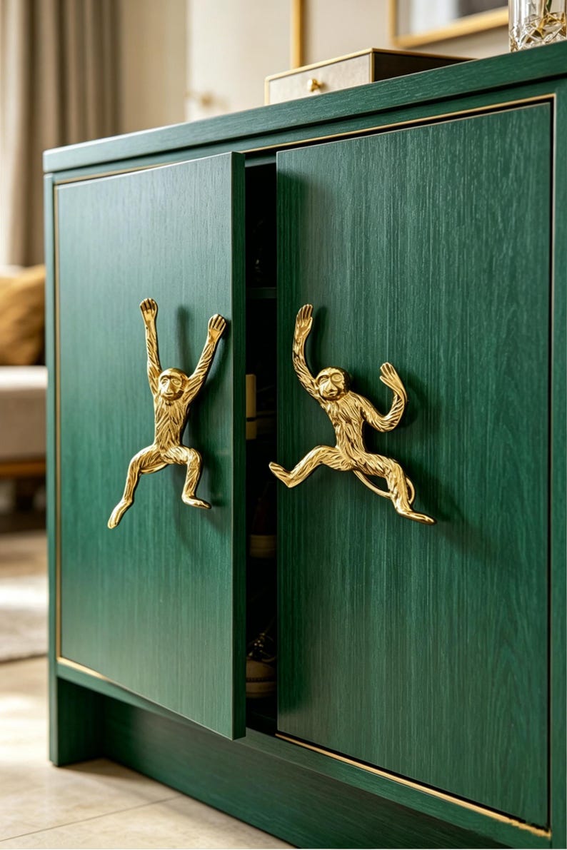 K&ouml;nnte beinhalten: Ein dunkelgr&uuml;ner Holzschrank mit zwei T&uuml;ren und goldfarbenen, affenf&ouml;rmigen Metallgriffen. Der Schrank weist eine sichtbare Holzmaserung und eine d&uuml;nne goldene Verzierung an den T&uuml;rkanten auf. Die Affengriffe sind in dynamischen Posen gestaltet.