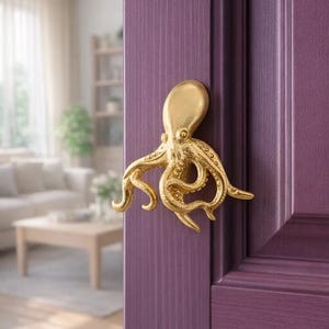Op de afbeelding: Een goudkleurige deurklink in de vorm van een octopus, gemonteerd op een paarse deur. De deurklink is een gedetailleerde sculptuur van een octopus met uitgestrekte tentakels. De deur heeft een rijke, effen paarse kleur.