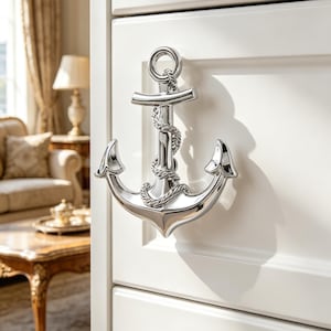 Peut inclure: Une poignée de meuble en forme d'ancre en chrome poli. La quincaillerie sur le thème nautique présente un motif de corde détaillé et est montée sur une porte d'armoire blanche. La conception de l'ancre comprend un anneau en haut et des bras incurvés.