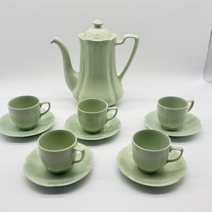 Peut inclure: Un service à thé vert pâle composé d'une grande théière avec couvercle et de quatre tasses assorties avec soucoupes. Chaque pièce présente une finition lisse de couleur unie avec un subtil motif à bords festonnés sur les soucoupes et le corps.