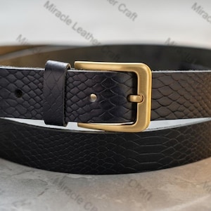 May include: A black leather belt with a textured snakeskin pattern. It has a gold-coloured rectangular buckle. The belt is coiled, displaying its design. The words "Miracle Leather Craft" are visible in the background.